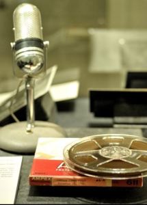 Levi Olan exhibition case showing a tape and its storage box in the forwground and a microphone in the background.